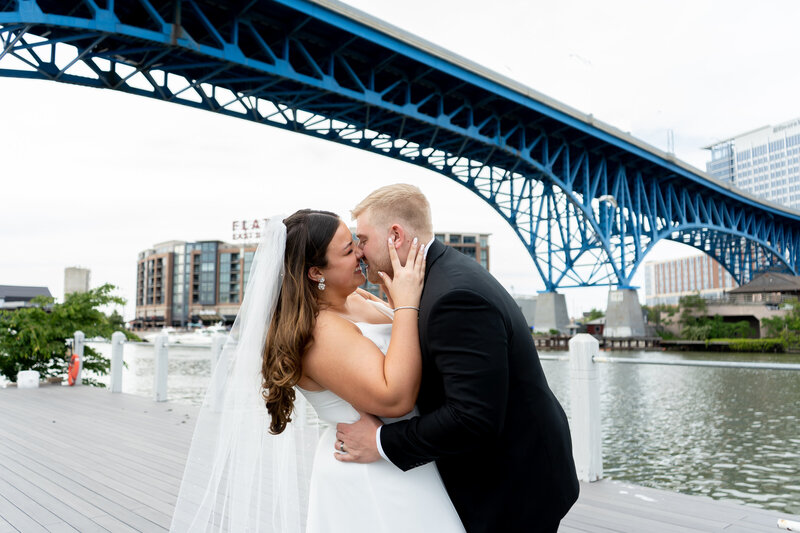 bride and groom kissing under bridge in Flats downtown Cleveland with soft evening glow on wedding day