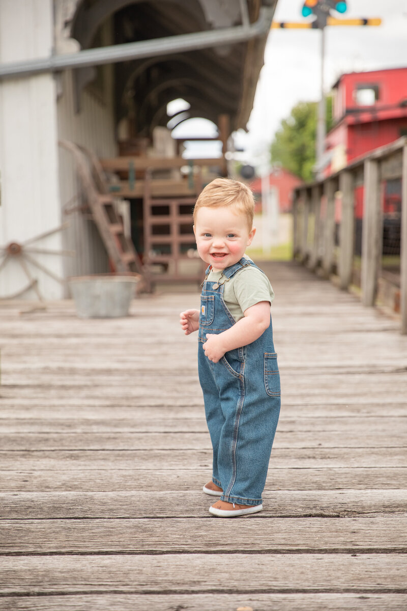 toddler boy smiles at camera while turning to walk on deck at train museum in saline michigan