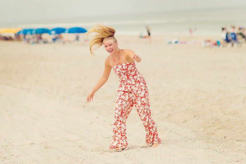 Jaeda on the beach for senior photos in a red summer jumpsuit after a cartwheel.
