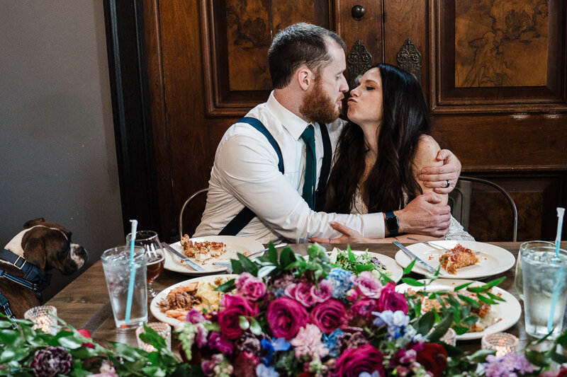 Bride and groom share a kiss at sweetheart table with floral centerpiece and their dog beside them – captured by Alex Kaplan, NJ wedding
