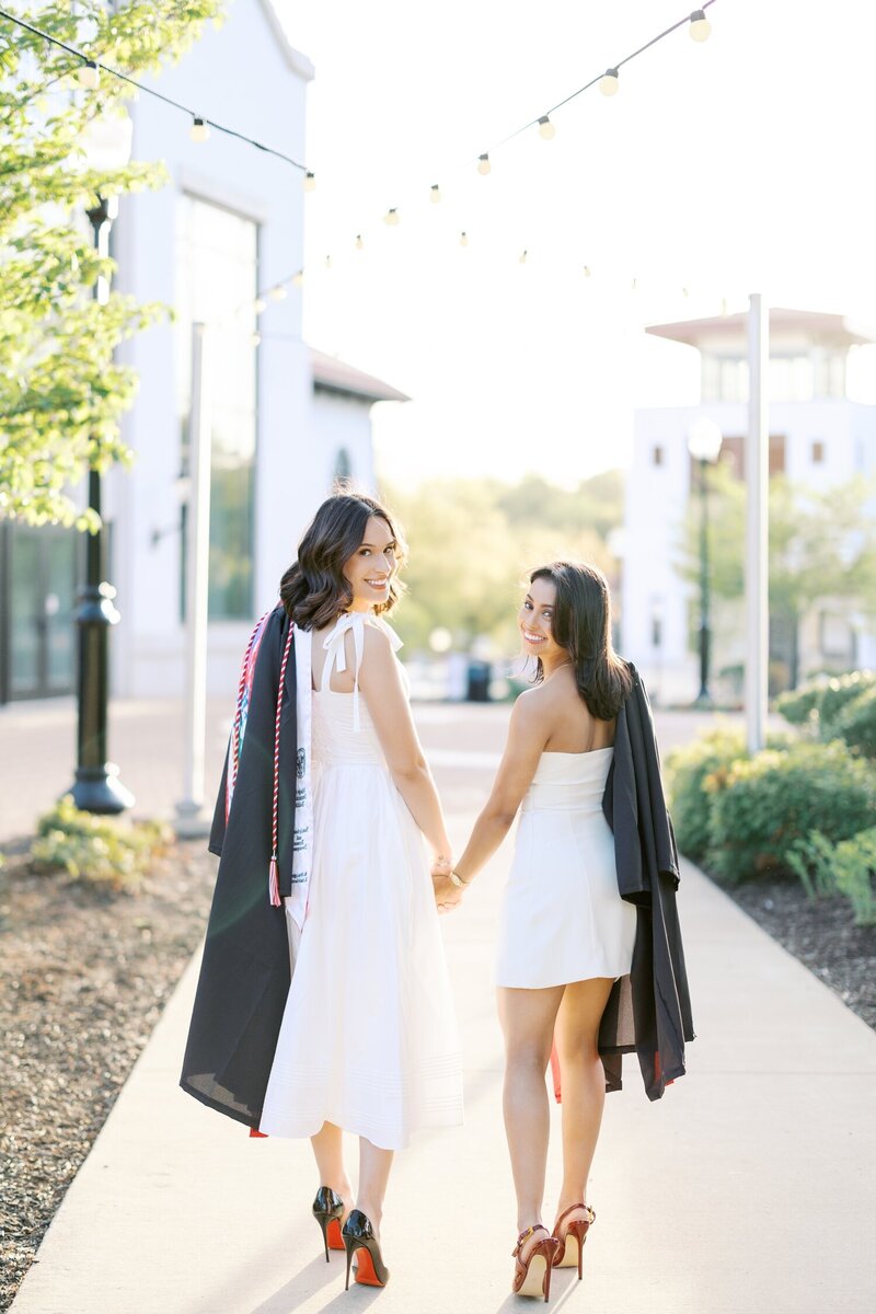 Two girls in white dresses holding hands and posing for senior photos