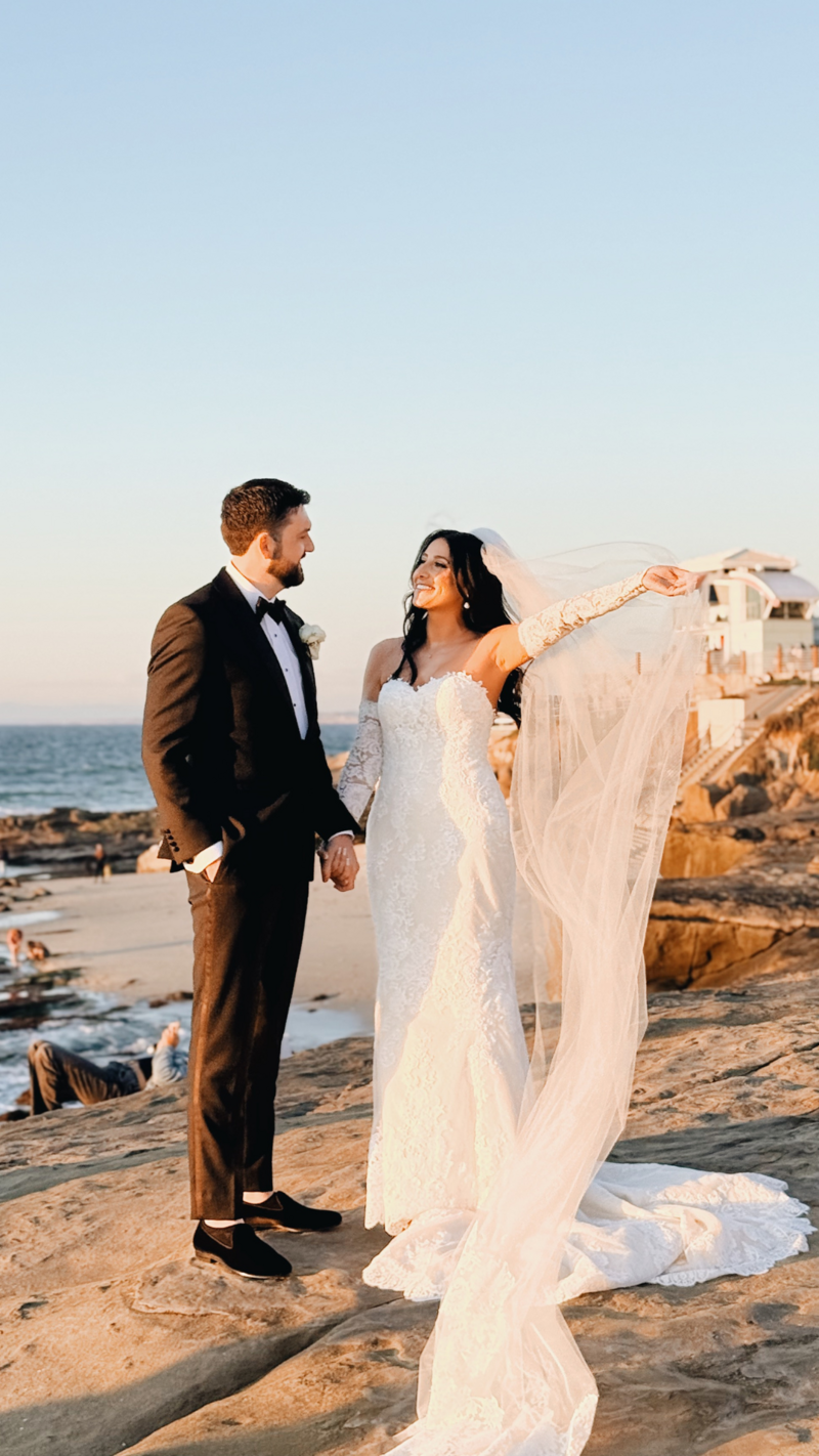 Bride and groom on the cliffs of La Jolla Beach letting the veil flow and holding hands.