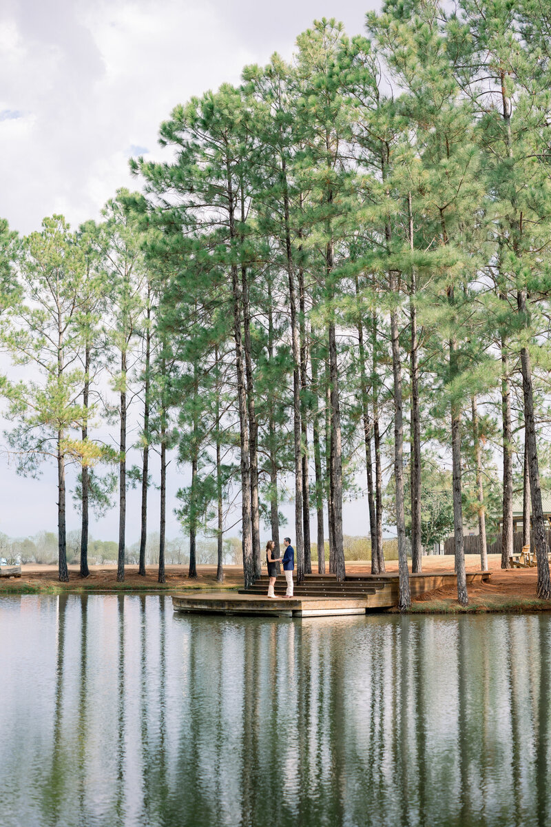 Man proposing to woman surrounded by pine trees and floral arrangements at Das Peach Haus in the Texas Hill Country — proposal photographed by Lois M Photography.