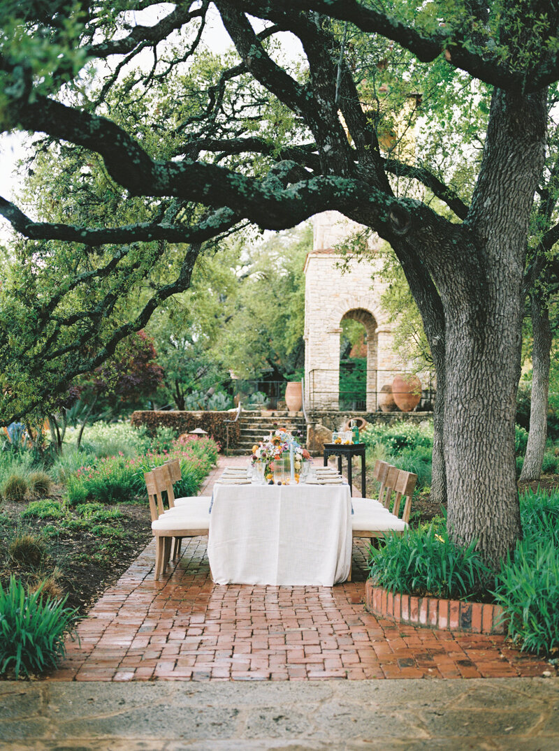 Spring tablescape with cream linen and colorful florals placed under tree on a brick pathway at Camp Lucy in Austin, Texas
