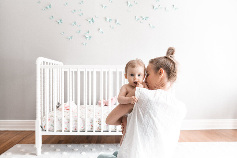 Hello & Co. Photography, mom in a babies nursery holding a toddler over her shoulder in front of a white crib
