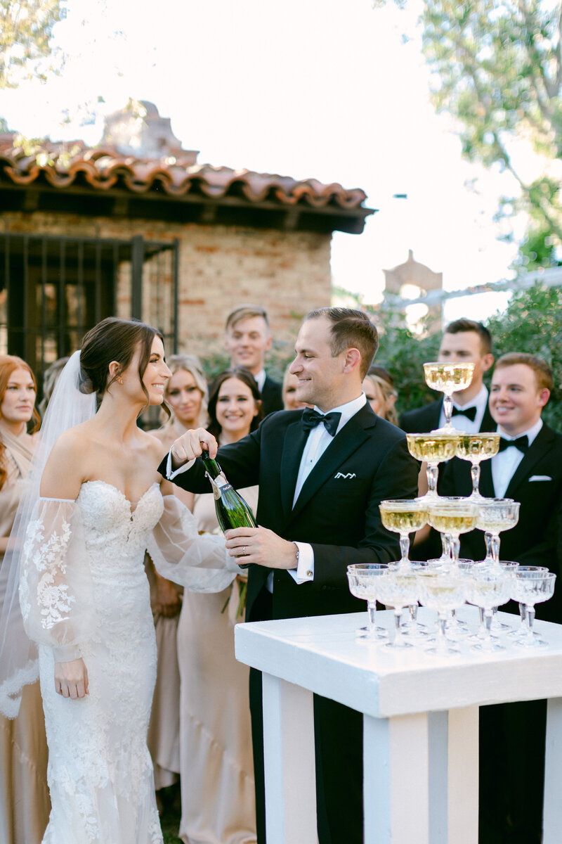Groom pops a bottle of champagne to pour over champagne tower with his bride