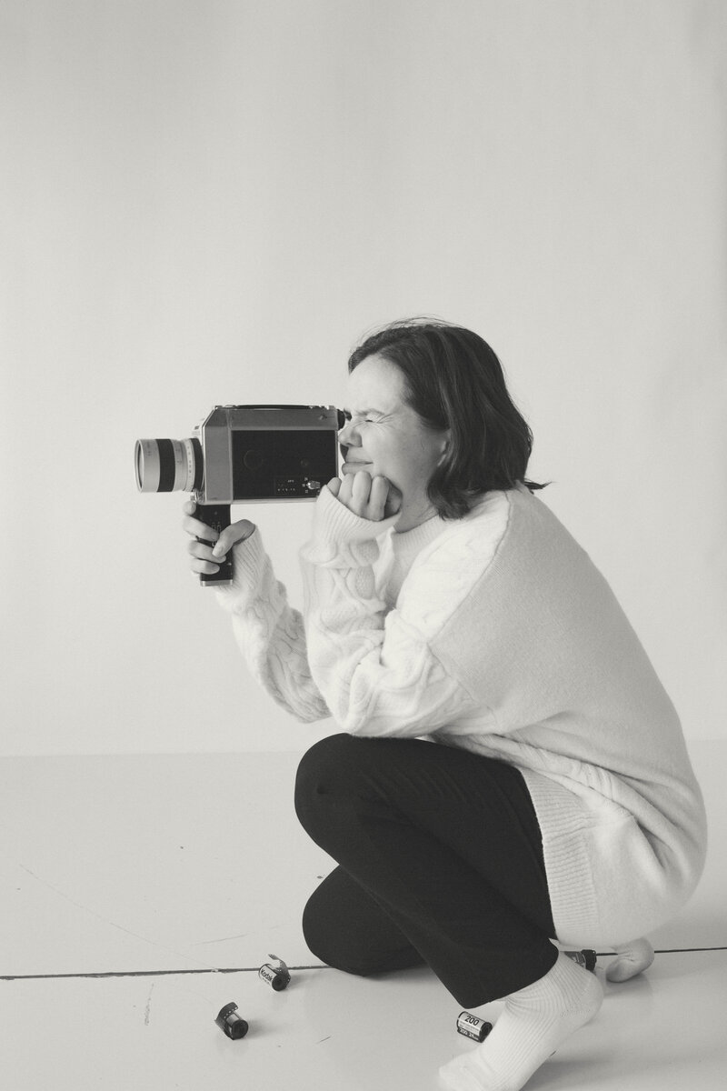 Photographer crouched down with camera gear and film, looking off thoughtfully during a personal photo session in Columbia, MO.