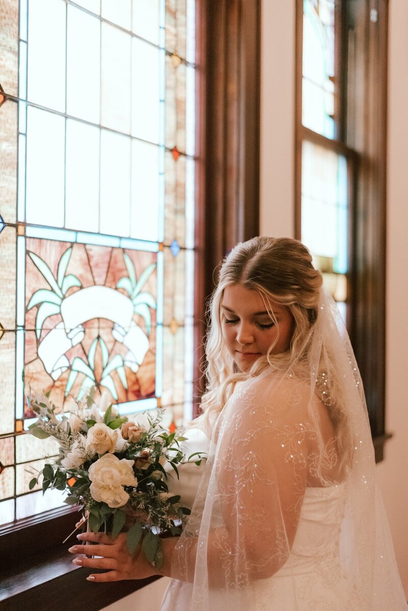 bride poses next to stained glass window on wedding day in peoria il