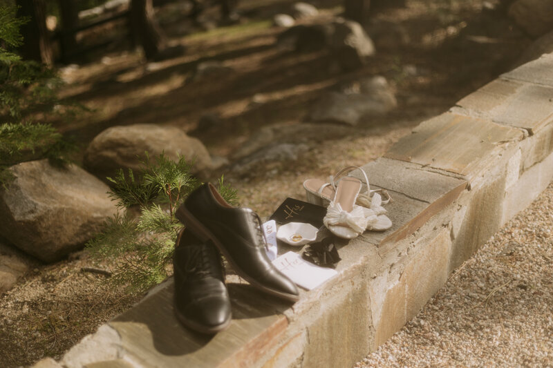 Details of the bride and grooms shoes resting on a ledge  with their vow books, rings, and bow tie.