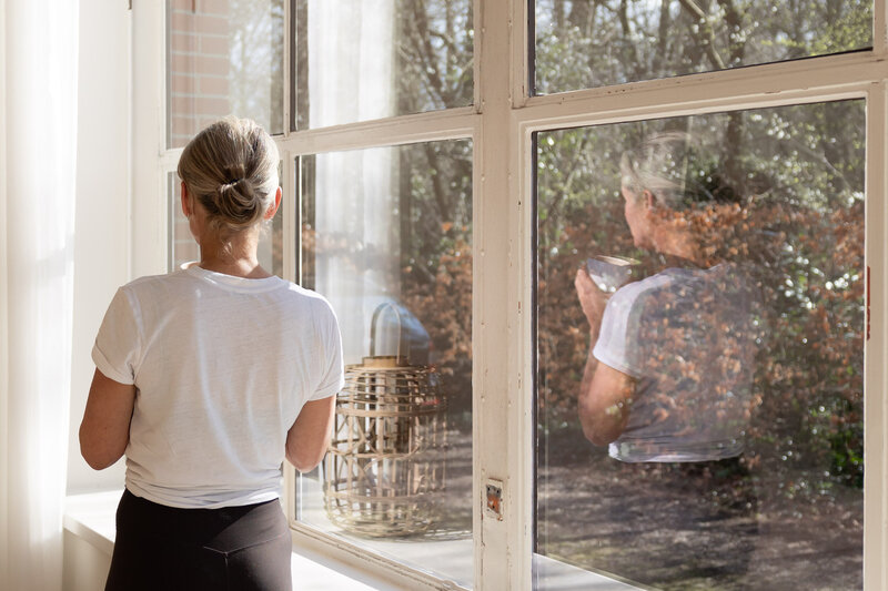 Spiegeling in raam van yoga studio waar docente kop thee drink en tot rust komt.