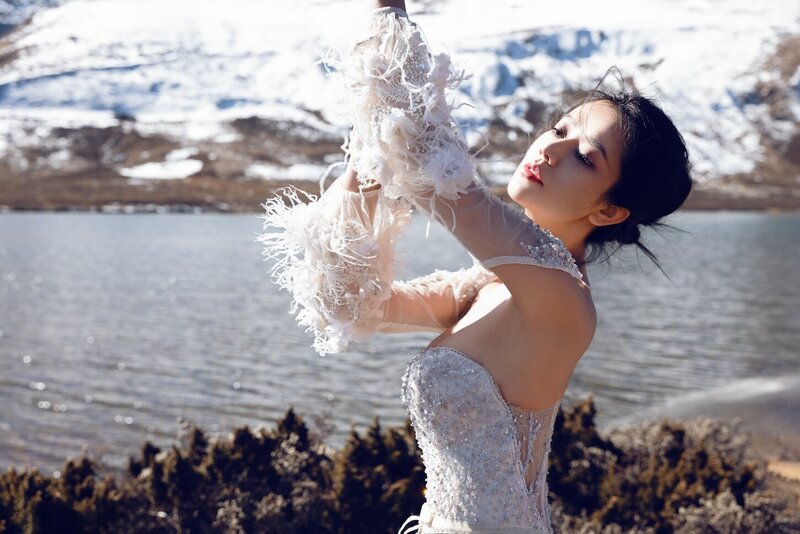 Dramatic shoot of a bride in a haute couture dress by an alpine lake in snow capped mountains.