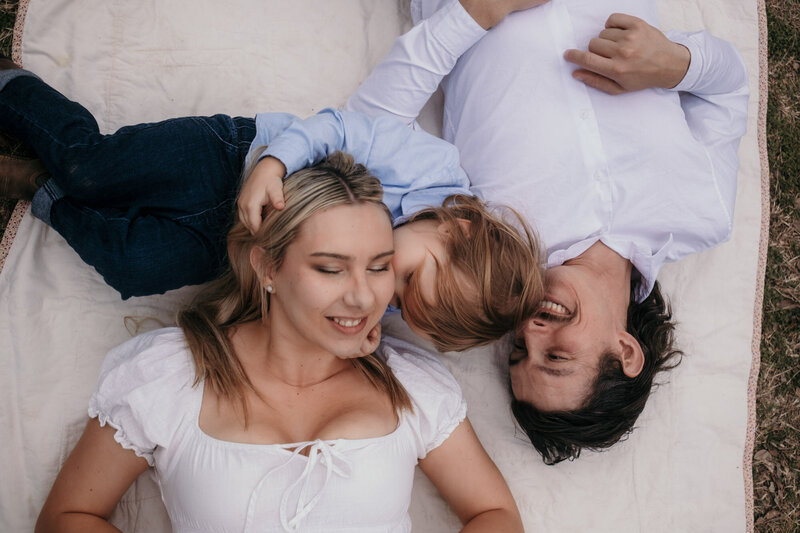 Boy kisses his mother laying besides the dad - Family Photos Karin Busch Los Angeles.