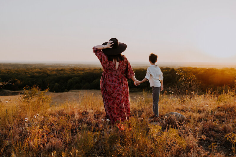Mother holds her son's hand while they look off into the sunset.