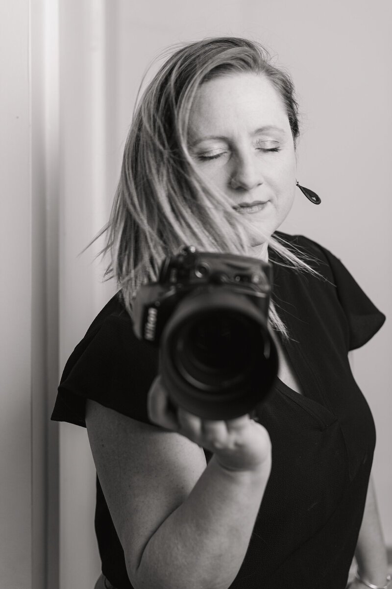 Creative black and white Headshot of Boston Personal Branding Photographer Kristin Palkoner, owner of Lens and Prism Photography, swirling hair and holding Nikon D700 camera.