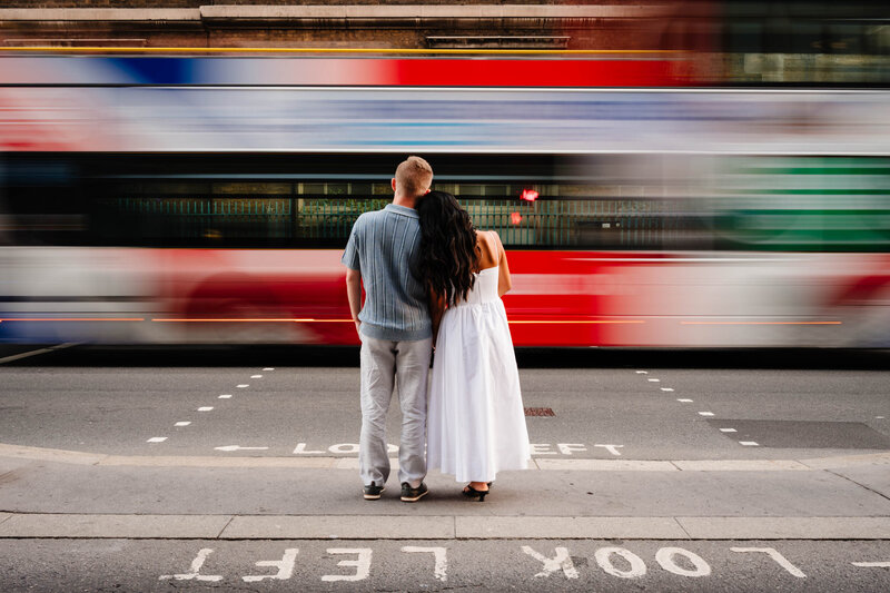 Couple waiting at the traffic light while blurred bus passes in front of them.