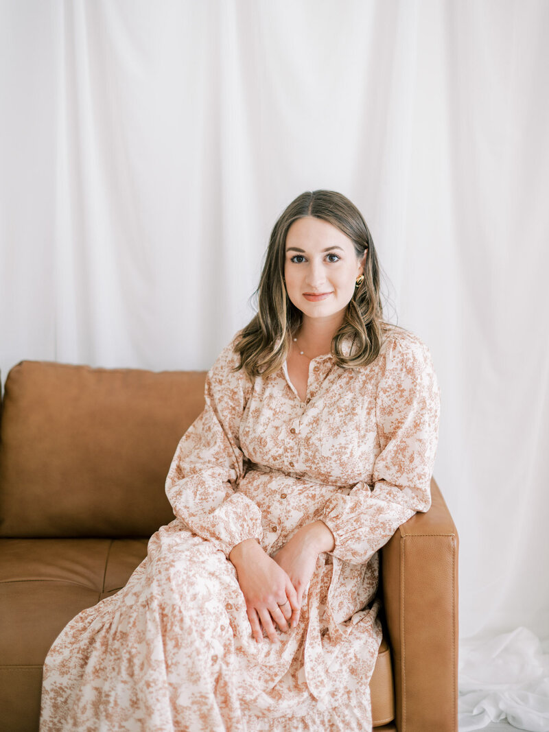 Calligraphy artist McKenna sits on a brown leather couch and looks at the camera