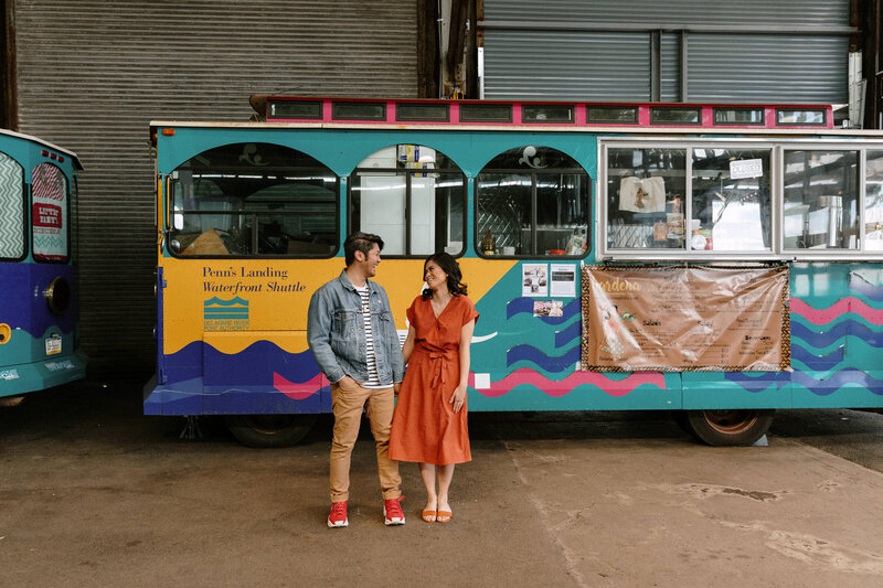 A couple beams with joy as they stand in front of a lively, colorful trolley, creating a memorable snapshot.