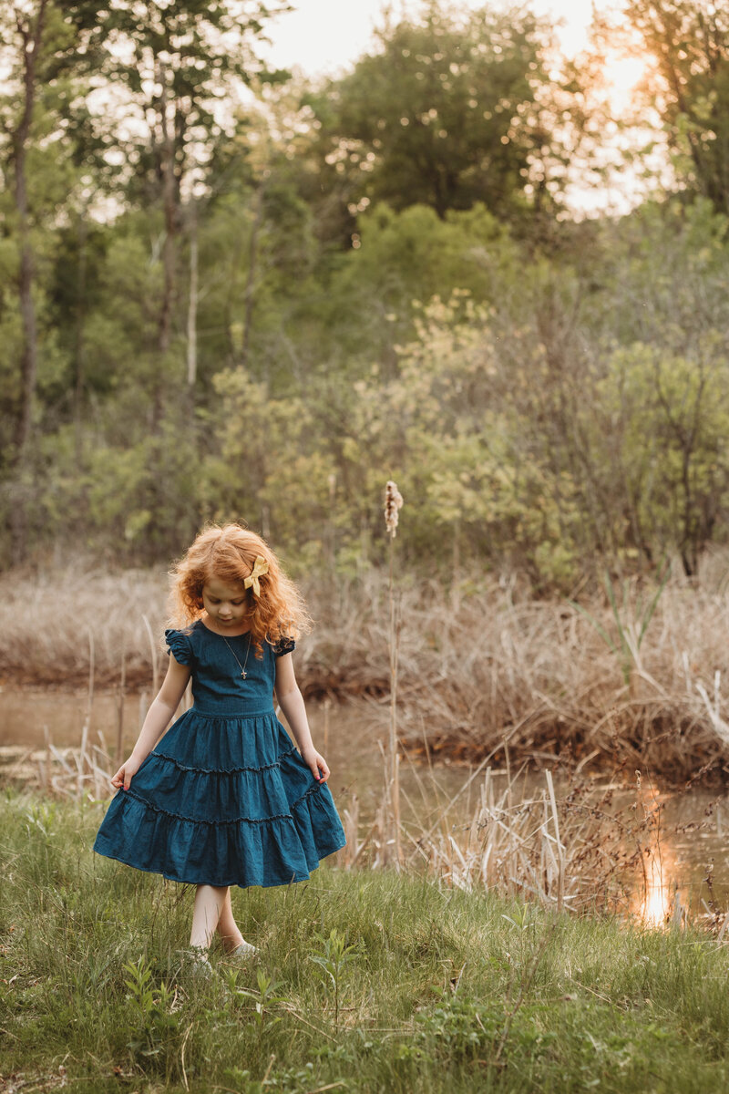 A little girl in a field holding her blue dress by a creek in Blacksburg, Virginia.