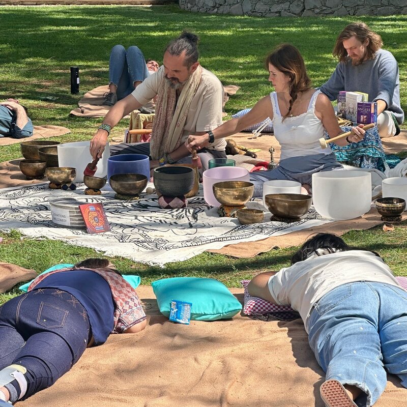 Two wellness practitioners lead a sound healing session outdoors, surrounded by singing bowls and participants lying on mats during the San Miguel Writers Conference wellness program.
