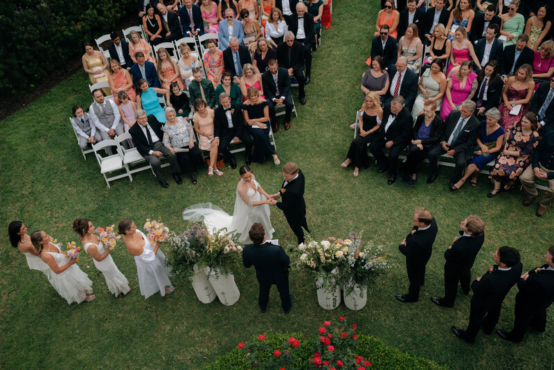 Aerial photo of bride and groom holding hands during their wedding ceremony with all of the guests watching them from their seats