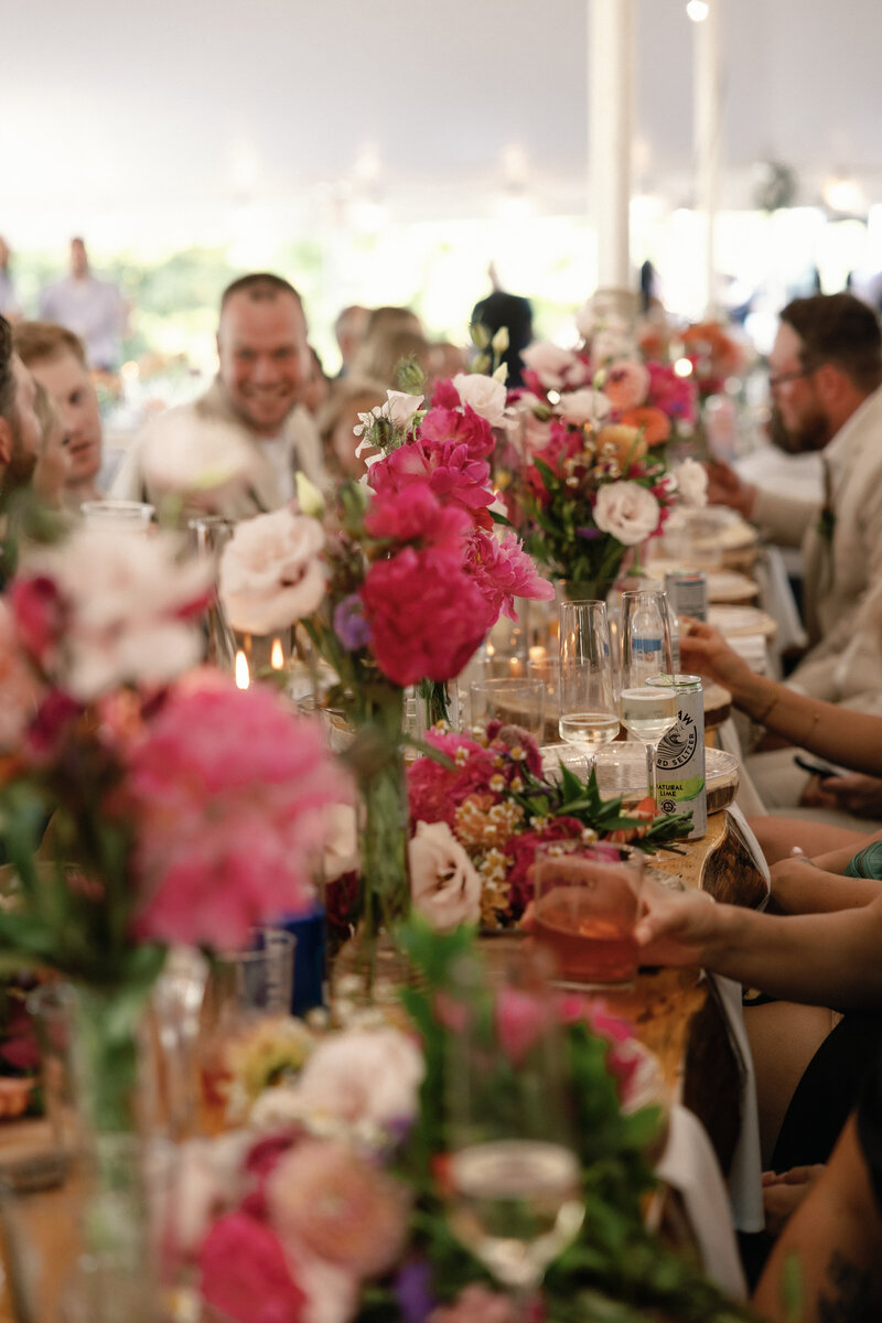 Four bridesmaids smile on a porch, holding vibrant bouquets as they look at the bride. A flower girl stands in front. They wear mismatched dresses in rich tones, creating a warm, elegant wedding moment.