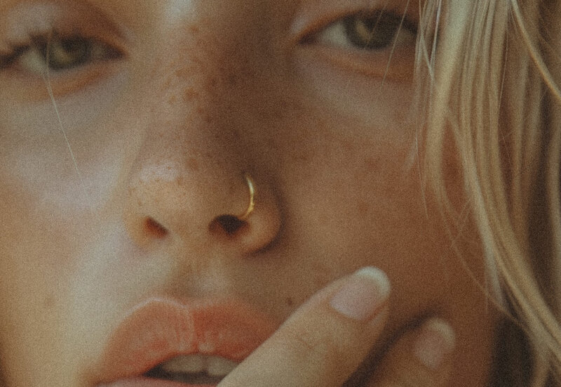 Close-up of a person's face with light freckles, a gold nose ring, slightly parted lips, and a hand touching their cheek—capturing the authentic style behind Sweet Pea Ink Creative’s brand strategy.