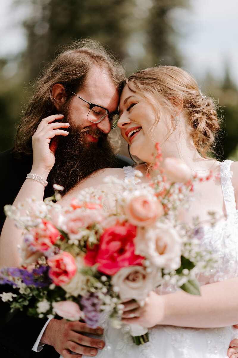 A groom kissing his bride's cheek while she closes her eyes and holds her bouquet.
