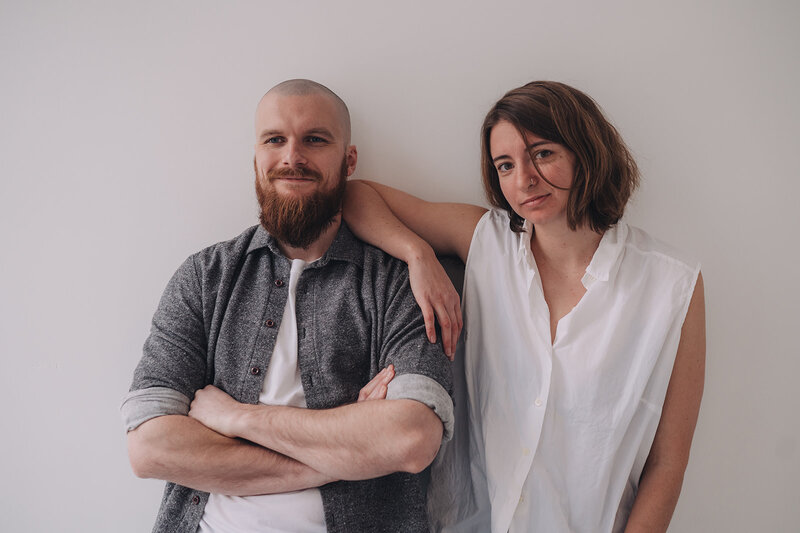 Marisa and Tanner of Msav Creative Co sit next to one another on the floor and smile at each other