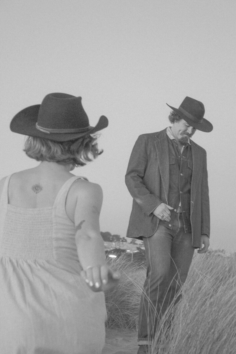 cowboy aesthetic playful engagement photos in oceanside california with couple running and playing in the sand