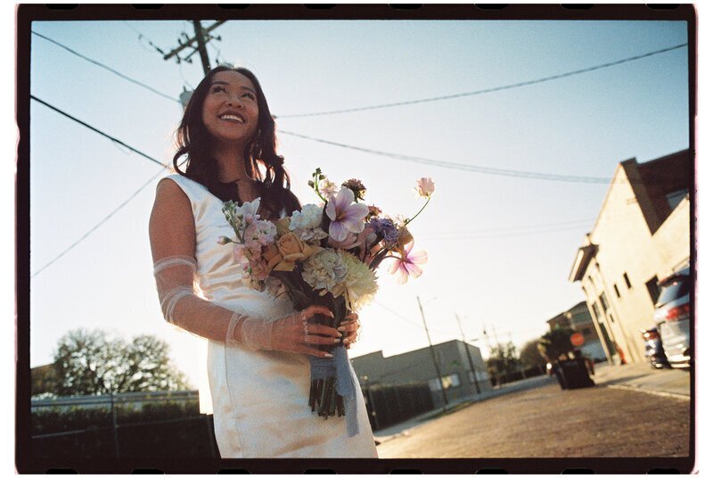 Bride posing with flowers on street by film wedding photographers Noble Photo Co