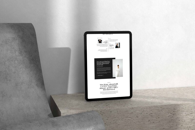 A tablet displaying a webpage from our editorial Showit template for coaches is placed on a light-colored stone surface next to a gray chair. Sunlight casts a shadow on the wall behind it.