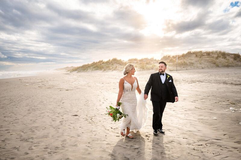 Bride and groom, holding hands while walking on the beach at Sunset, outside of Icona Windrift hotel in Avalon, New Jersey