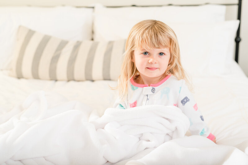 Toddler girl sitting on bed under a blanket