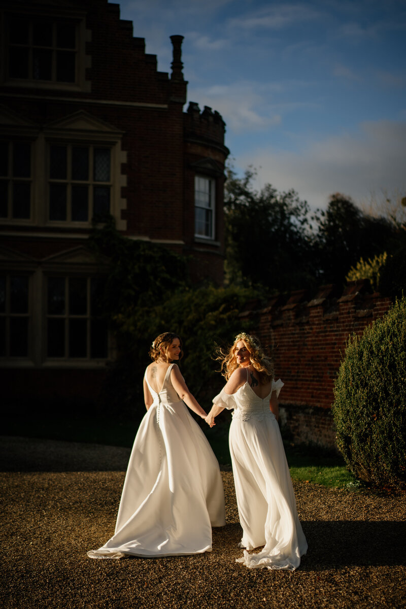 Two brides holding hands at sunset on their wedding day in Suffolk