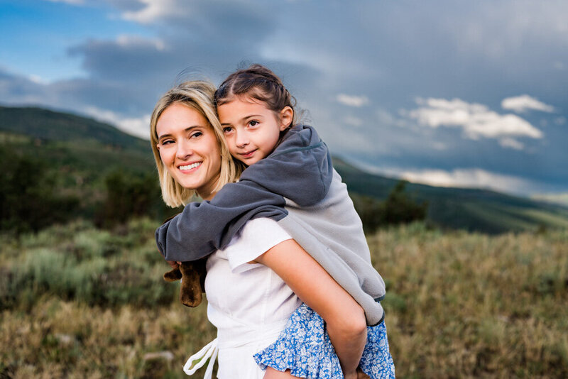 A mom gives her daughter a piggy back ride in a field