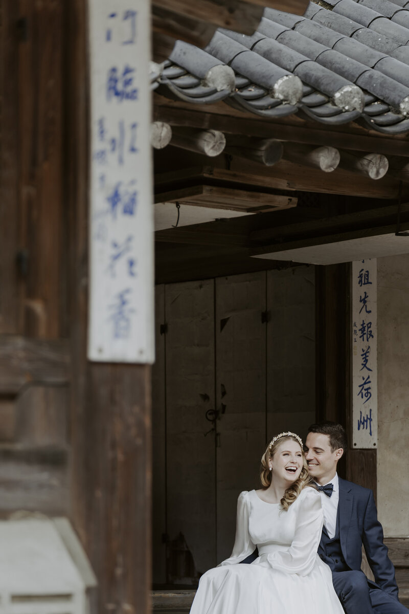bride wearing a white dress and gold hairband and groom wearing a blue tuxedo smile during after eloping in Seoul,