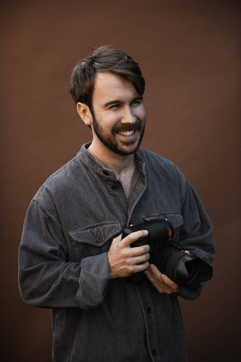 Portrait of Tom Keenan smiling while holding a camera.