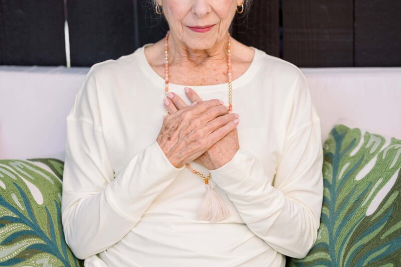Close up of a woman sitting peacefully with both hands over her heart.