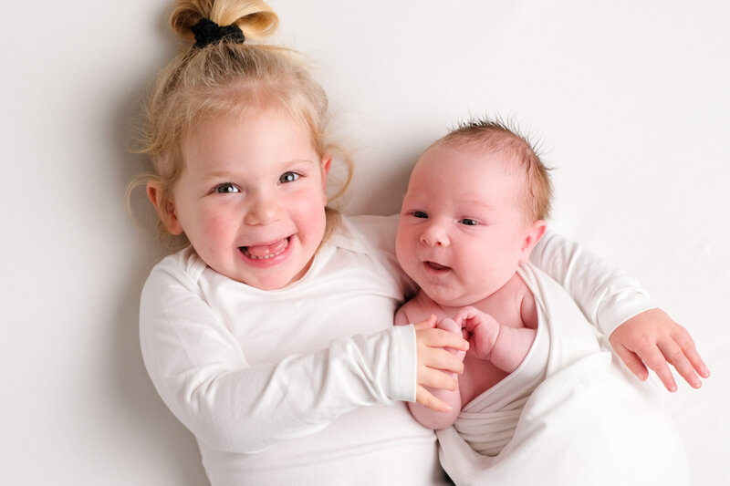 Een pure en liefdevolle foto van pasgeboren baby samen met grote zus. Perfect vastgelegd tijdens een newborn shoot aan huis.