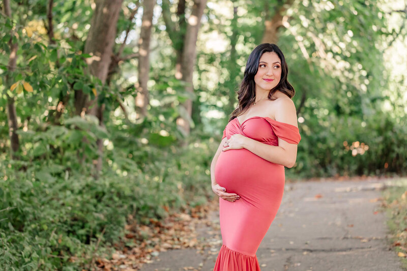 An outdoor photography session of a mother-to-be in a fitted pink dress.