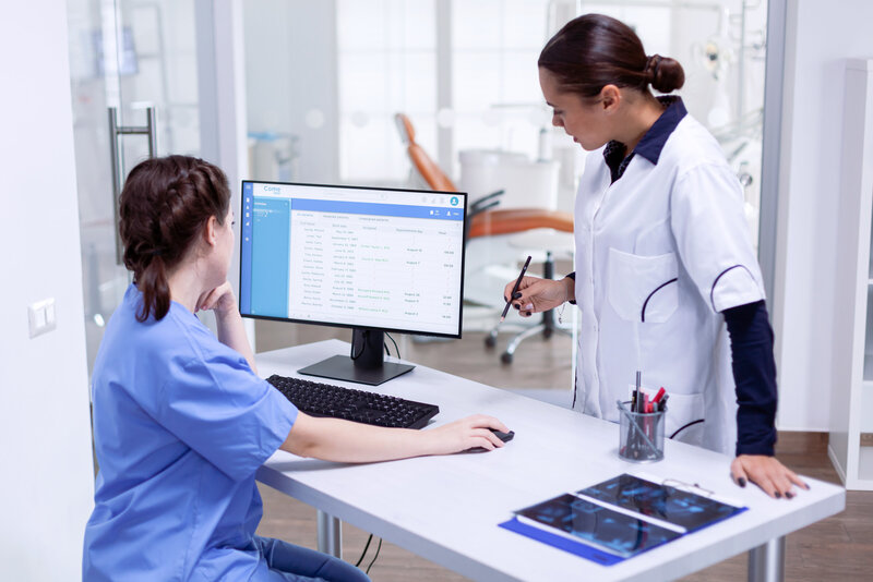 Two dentists discussing work while looking at a computer monitor.