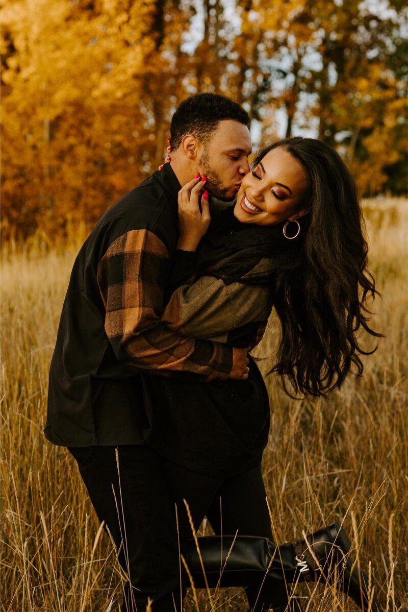 Man kisses his fiance on the cheek during their engagement session.