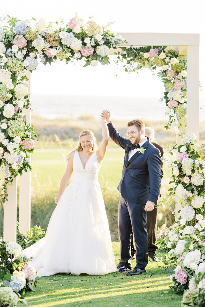 Bride and groom cheering under floral arch at the ocean course