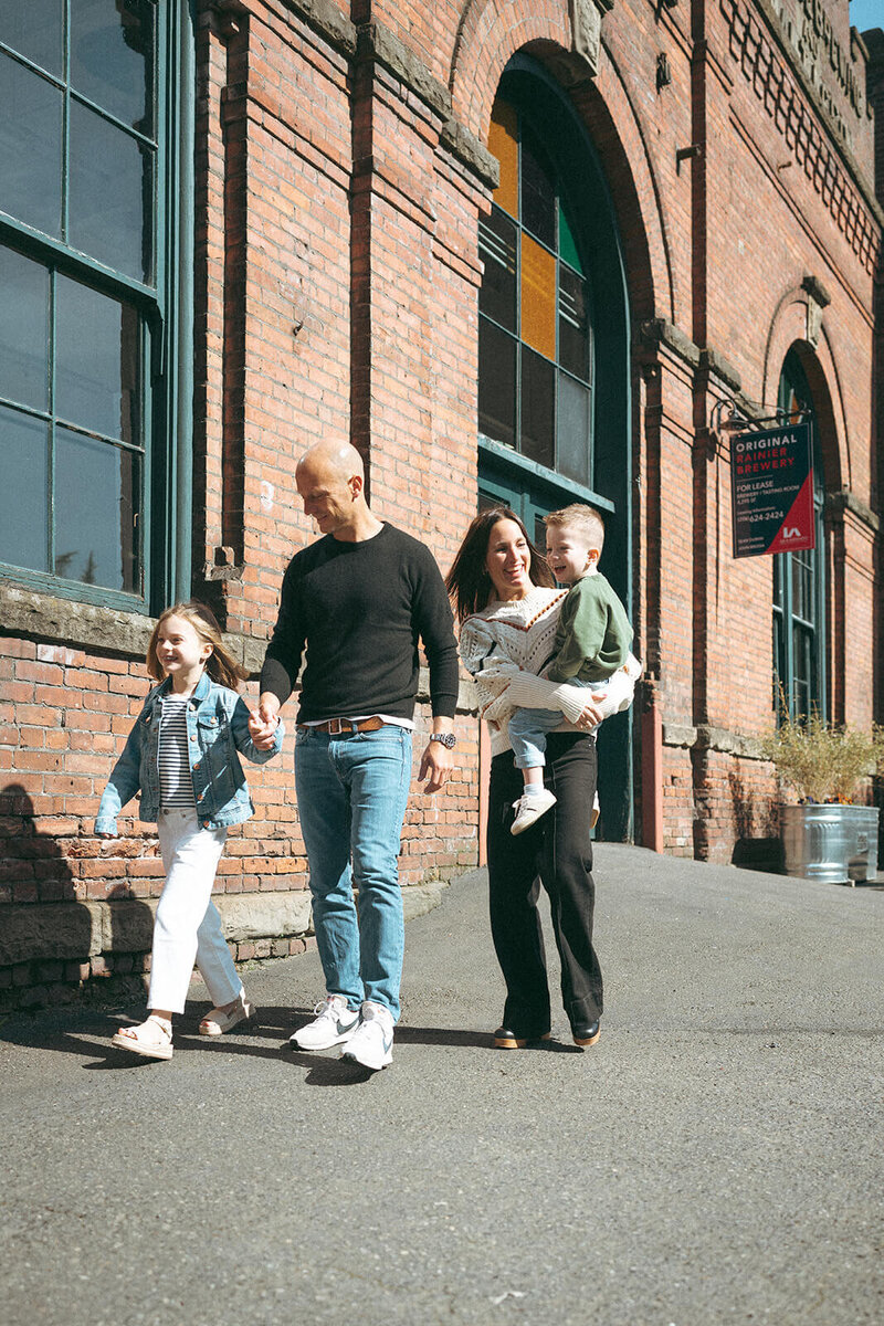 Candid family walking together along brick building during urban lifestyle photo session in Orange County