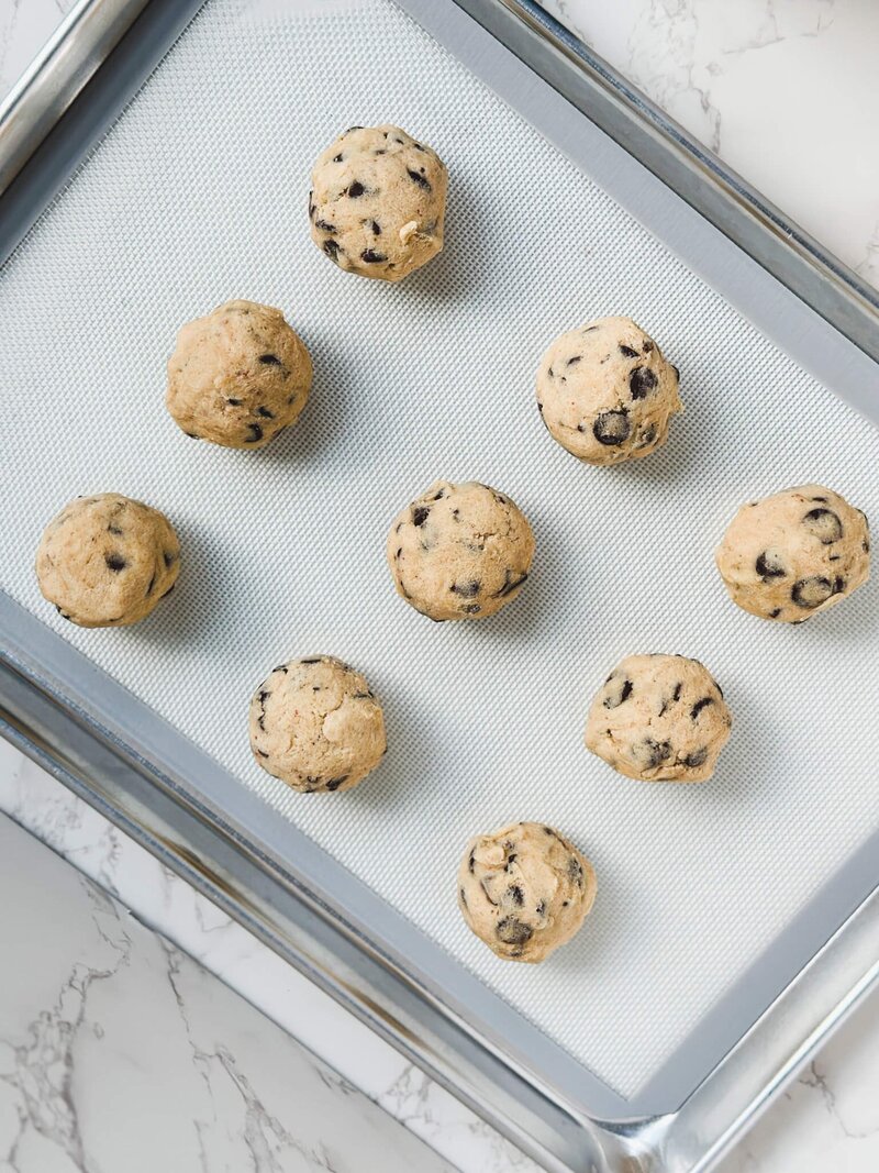 Fresh chocolate chip cookie dough arranged neatly on a baking sheet, ready for the oven.