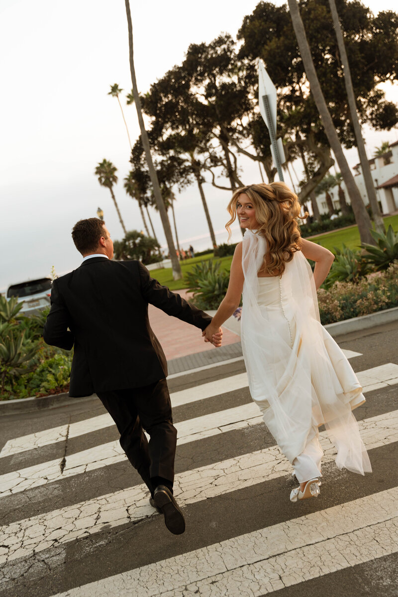a bride and groom running across a crosswalk towards the ocean