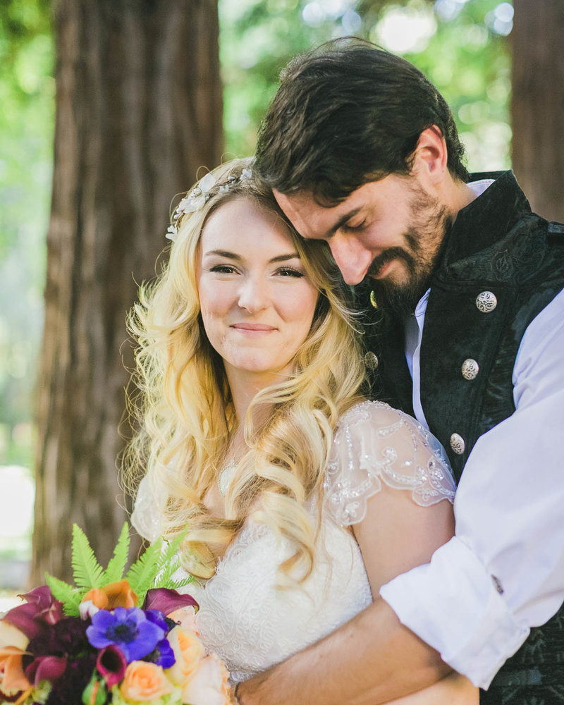 Groom stands behind Bride hugging her as she smiles towards the camera