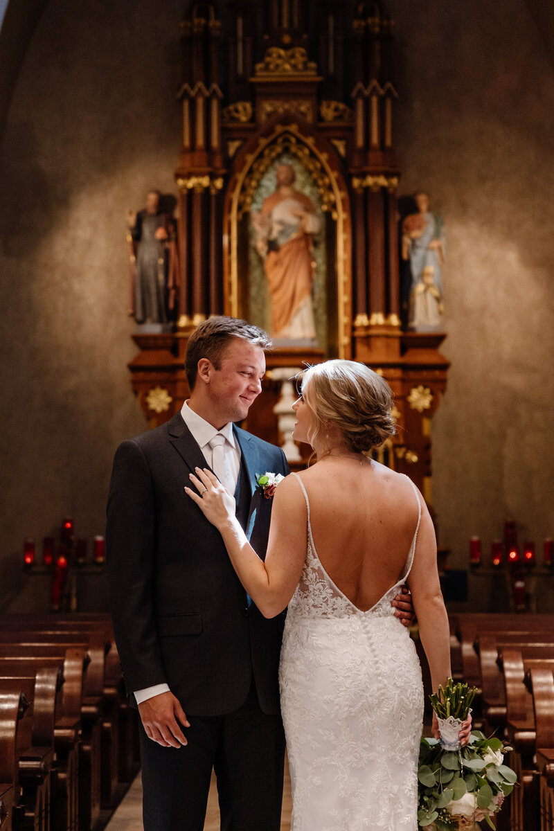 A newlywed couple standing close together smiling at each other in a church