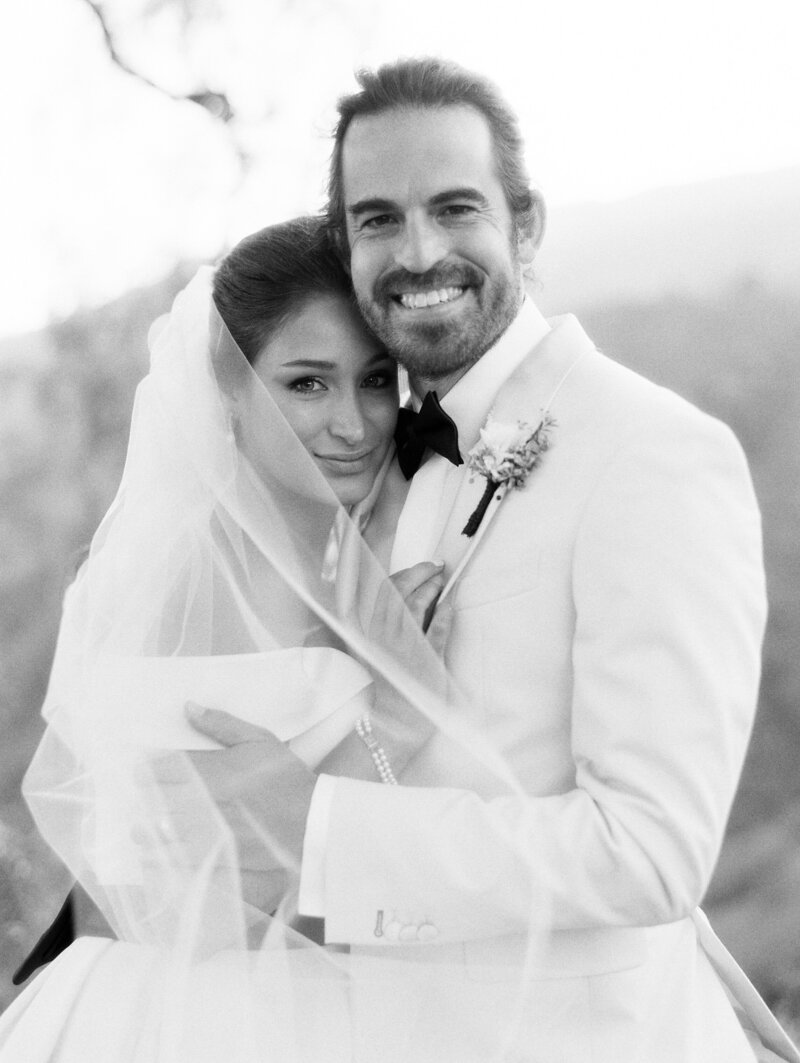 black and white wedding photo of couple wrapped in veil