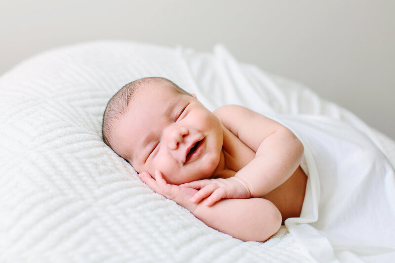 A baby smiling while laying on a white blanket during her newborn session with Camarillo photographer Daniele Rose